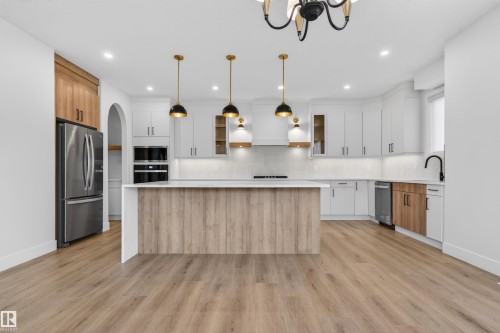 Kitchen featuring a central island with wood-finish paneling, white countertops, stainless steel appliances, white cabinetry, and wood-finish flooring - 27 Redpoll Wynd, St. Albert, AB - Indoor Photo Showing Kitchen With Upgraded Kitchen