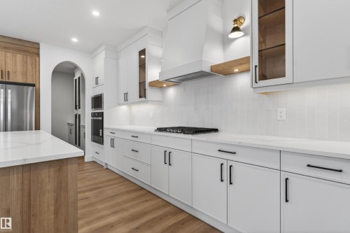 Modern kitchen featuring white cabinetry, light countertops, wood-finish flooring, a built-in range, and a stainless steel refrigerator - 27 Redpoll Wynd, St. Albert, AB - Indoor Photo Showing Kitchen With Upgraded Kitchen