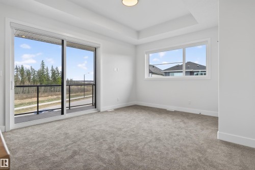 Spacious room featuring a tray ceiling, plush carpet flooring, a large window, and a glass-paneled sliding door opening to a private balcony with black railings - 27 Redpoll Wynd, St. Albert, AB - Indoor Photo Showing Other Room