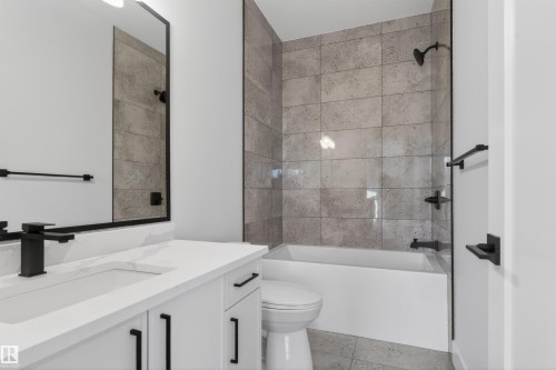Bathroom featuring a white vanity with integrated sink, matte black fixtures, a rectangular mirror, a bathtub with a tiled surround, and coordinating floor tiles - 27 Redpoll Wynd, St. Albert, AB - Indoor Photo Showing Bathroom