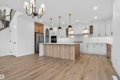 Kitchen featuring a large island with wood-finish paneling, white cabinetry, integrated stainless steel appliances, pendant lighting, and wood-finish flooring - 27 Redpoll Wynd, St. Albert, AB - Indoor Photo Showing Kitchen With Upgraded Kitchen