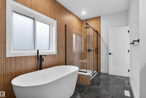 Freestanding soaking tub with a matte black floor-mounted faucet, complemented by wood-finish wall paneling - 27 Redpoll Wynd, St. Albert, AB - Indoor Photo Showing Bathroom