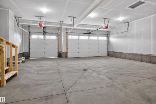 Spacious multi-bay garage featuring two overhead doors with window accents, concrete flooring, and an unfinished ceiling with recessed lighting - 27 Redpoll Wynd, St. Albert, AB - Indoor Photo Showing Garage