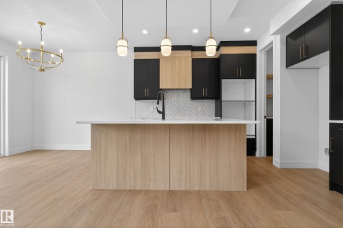 Kitchen featuring dark cabinetry, an island with sink, light wood-style flooring, and suspended lighting - 19 Rosa Crescent, St. Albert, AB - Indoor Photo Showing Kitchen