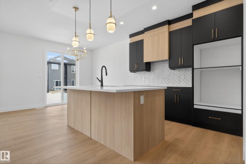 Kitchen with two tone color scheme, tasteful backsplash, light wood finished floors, a center island with sink, and a chandelier - 19 Rosa Crescent, St. Albert, AB - Indoor Photo Showing Kitchen