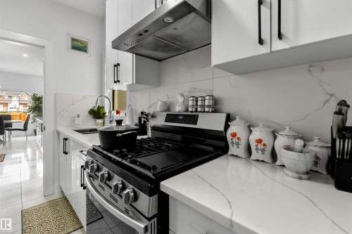 Kitchen featuring white cabinetry, stainless steel range with gas cooktop, extractor fan, and light stone counters - 15518 13A Avenue, Edmonton, AB - Indoor Photo Showing Kitchen