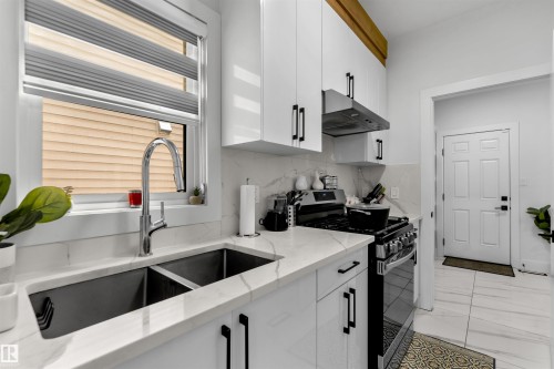 Kitchen featuring gas stove, white cabinetry, under cabinet range hood, light stone counters, and decorative backsplash - 15518 13A Avenue, Edmonton, AB - Indoor Photo Showing Kitchen With Double Sink
