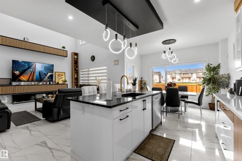 Kitchen featuring white cabinetry, pendant lighting, open floor plan, a kitchen island with sink, and modern cabinets - 15518 13A Avenue, Edmonton, AB - Indoor