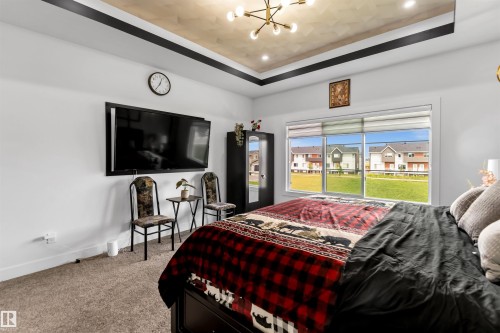Bedroom with a raised ceiling, carpet flooring, a chandelier, and a residential view - 15518 13A Avenue, Edmonton, AB - Indoor Photo Showing Bedroom