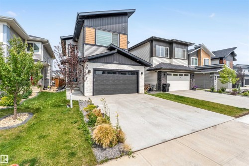 View of front of property with stone siding, a garage, board and batten siding, driveway, and a front lawn - 15518 13A Avenue, Edmonton, AB - Outdoor With Facade