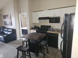 Kitchen with black appliances, white cabinetry, under cabinet range hood, dark colored carpet, and dark countertops - 