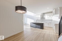 Kitchen with white cabinetry, a center island with sink, wall chimney range hood, hanging light fixtures, and light wood-style floors - 