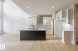 Kitchen with an island with sink, white cabinetry, decorative backsplash, wall chimney range hood, and recessed lighting - 