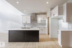 Kitchen with white cabinets, backsplash, wall chimney range hood, a center island with sink, and light wood finished floors - 