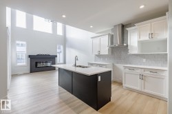 Kitchen featuring decorative backsplash, white cabinetry, wall chimney exhaust hood, a kitchen island with sink, and plenty of natural light - 