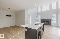 Kitchen featuring open floor plan, pendant lighting, light wood-style flooring, a glass covered fireplace, and a kitchen island with sink - 