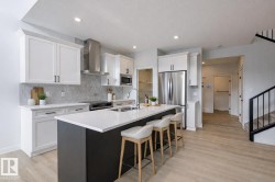 Kitchen featuring wall chimney exhaust hood, stainless steel appliances, tasteful backsplash, a center island with sink, and recessed lighting - 