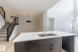 Kitchen featuring light wood-style flooring, a kitchen island with sink, hanging light fixtures, light stone counters, and a towering ceiling - 