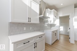 Kitchen featuring wall chimney range hood, white cabinetry, tasteful backsplash, and light wood finished floors - 