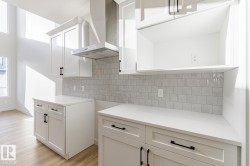 Kitchen with wall chimney exhaust hood, white cabinetry, light wood-style floors, and decorative backsplash - 