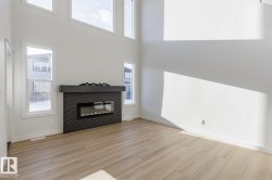 Unfurnished living room featuring a glass covered fireplace, light wood-style flooring, and a towering ceiling - 