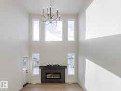 Unfurnished living room featuring light wood-style flooring, healthy amount of natural light, a glass covered fireplace, and a towering ceiling - 