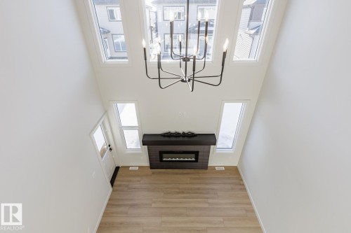 Unfurnished living room with light wood-style flooring, a glass covered fireplace, a towering ceiling, and a chandelier - 3719 42 Avenue, Beaumont, AB - Indoor Photo Showing Other Room