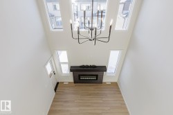 Unfurnished living room with light wood-style flooring, a glass covered fireplace, a towering ceiling, and a chandelier - 