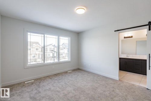 Unfurnished bedroom featuring a barn door, light carpet, and ensuite bath - 3719 42 Avenue, Beaumont, AB - Indoor Photo Showing Other Room