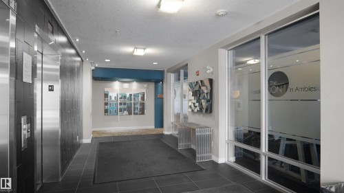 Corridor featuring dark tile patterned floors, elevator, and a textured ceiling - 105 2584 Anderson Way, Edmonton, AB - Indoor Photo Showing Other Room