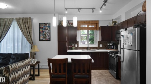 Kitchen with appliances with stainless steel finishes, light countertops, dark brown cabinetry, pendant lighting, and decorative backsplash - 105 2584 Anderson Way, Edmonton, AB - Indoor Photo Showing Kitchen