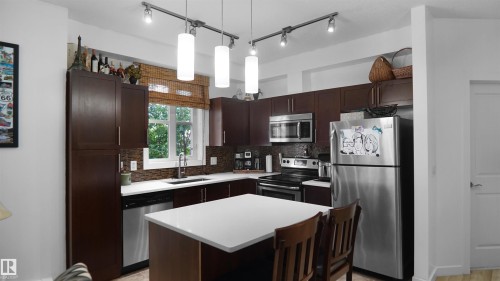 Kitchen with appliances with stainless steel finishes, dark brown cabinetry, pendant lighting, a kitchen island, and a kitchen breakfast bar - 105 2584 Anderson Way, Edmonton, AB - Indoor Photo Showing Kitchen
