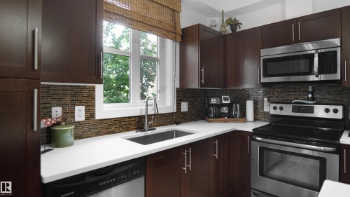 Kitchen with dark brown cabinetry, appliances with stainless steel finishes, and tasteful backsplash - 105 2584 Anderson Way, Edmonton, AB - Indoor Photo Showing Kitchen With Upgraded Kitchen