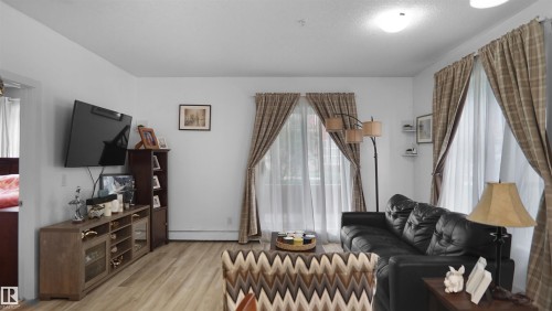 Living room with plenty of natural light, light wood-style floors, and a baseboard heating unit - 105 2584 Anderson Way, Edmonton, AB - Indoor Photo Showing Other Room