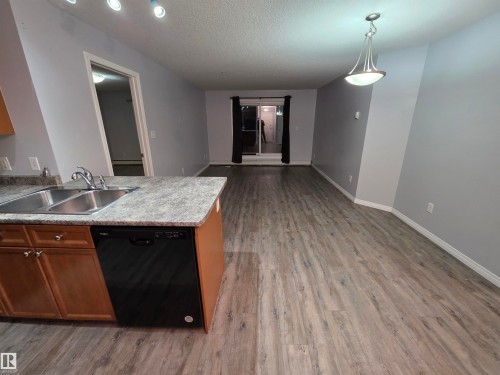 Kitchen featuring black dishwasher, open floor plan, decorative light fixtures, light wood-style floors, and light countertops - 106 4903 47 Avenue, Stony Plain, AB - Indoor Photo Showing Kitchen With Double Sink