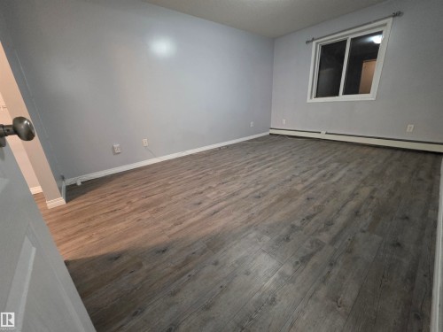 Unfurnished room with dark wood-style floors and a baseboard heating unit - 106 4903 47 Avenue, Stony Plain, AB - Indoor Photo Showing Other Room