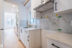 Kitchen with white cabinets, under cabinet range hood, light stone counters, decorative backsplash, and modern cabinets - 