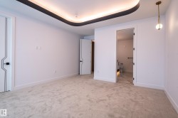 Unfurnished bedroom with light carpet, ensuite bathroom, and a tray ceiling - 