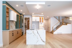 Kitchen with a center island with sink, glass insert cabinets, light stone counters, white cabinets, and light wood-type flooring - 