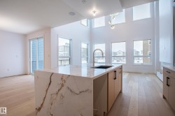 Kitchen with light stone counters, light wood-type flooring, a center island with sink, and modern cabinets - 