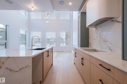Kitchen featuring light stone counters, under cabinet range hood, backsplash, and modern cabinets - 