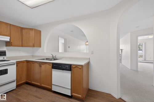 Kitchen featuring white appliances, light countertops, under cabinet range hood, and dark wood-style floors - 106 15499 Castle Downs Road, Edmonton, AB - Indoor Photo Showing Kitchen With Double Sink
