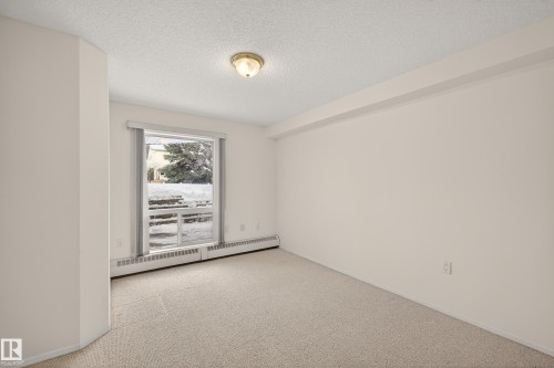 Empty room with a baseboard radiator, a textured ceiling, and light carpet - 106 15499 Castle Downs Road, Edmonton, AB - Indoor Photo Showing Other Room