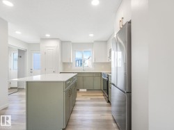 Kitchen with stainless steel appliances, a center island, white cabinetry, light wood finished floors, and green cabinets - 
