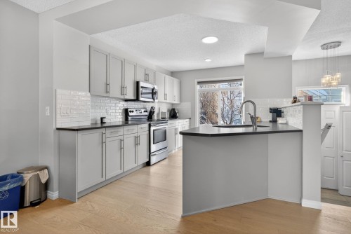 Kitchen featuring a textured ceiling, stainless steel appliances, a peninsula, light wood-style floors, and pendant lighting - 60 1804 70 Street, Edmonton, AB - Indoor Photo Showing Kitchen With Upgraded Kitchen