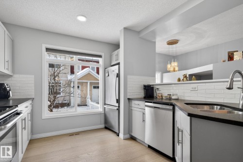 Kitchen featuring decorative backsplash, dark stone countertops, appliances with stainless steel finishes, light wood-style floors, and a textured ceiling - 60 1804 70 Street, Edmonton, AB - Indoor Photo Showing Kitchen