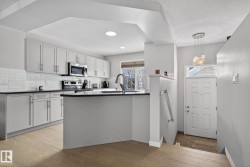 Kitchen with a textured ceiling, a peninsula, appliances with stainless steel finishes, light wood-style floors, and white cabinetry - 