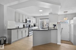 Kitchen with a textured ceiling, dark countertops, stainless steel appliances, a peninsula, and light wood-style floors - 