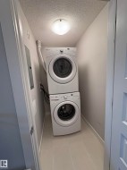 Laundry room with light tile patterned flooring, stacked washer and clothes dryer, electric panel, and a textured ceiling - 