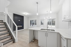 Kitchen with light stone counters, hanging light fixtures, light wood-style floors, white cabinetry, and a peninsula - 